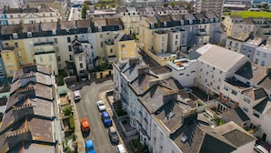 Zona residenziale con case a schiera e un alto edificio condominiale. Diverse auto sono parcheggiate lungo la strada, e si intravede un'area d'acqua sullo sfondo.