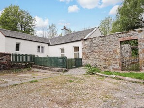 Ein rustikales Steinhaus mit weißer Fassade, einem grünen Zaun und einem Kopfsteinpflasterhof.