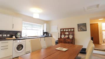 A compact kitchen with a washing machine, a dining table, and a wall-mounted dish rack.