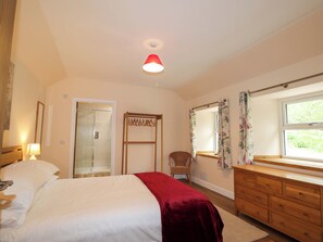 A bedroom with a bed, a dresser, a chair, a window with curtains, a mirror, and a ceiling light.