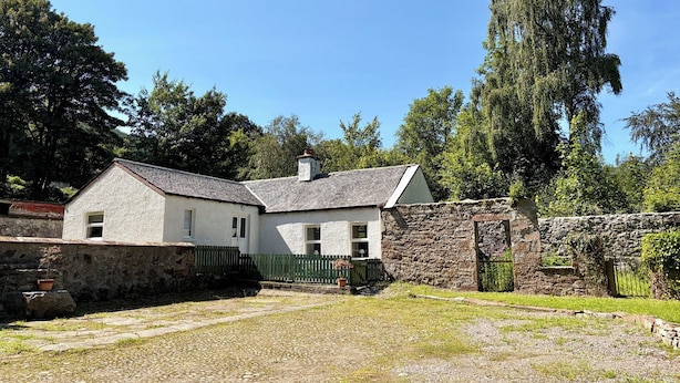 A two-story house with a stone wall and a wooden fence. - Laundry Cottage (Strathpeffer)