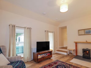 A living room with a TV, books, a fireplace, and a view of the outside. - Laundry Cottage (Strathpeffer)