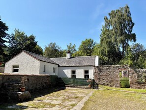 A traditional stone house with a sloped roof, a small porch, and a stone wall.
