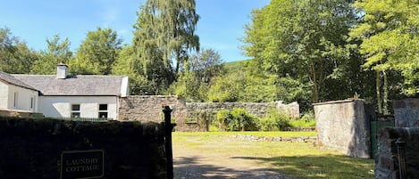 A rural property with a stone wall, a sign reading 'LAUNDRY COTTAGE,' and a gravel path leading to a grassy area.