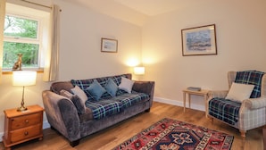 A cozy living room with a sofa, a chair, a small table, a lamp, and a rug. - Laundry Cottage (Strathpeffer)
