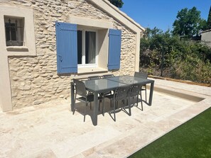 Ein Steinhäuschen mit Terrasse, einem Glastisch und blauen Fensterläden.