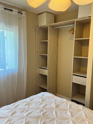 Ein Schlafzimmer mit einem Bett, einem Holzschrank und einem Fenster mit durchsichtigen Vorhängen.