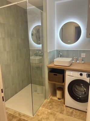 Ein modernes Badezimmer mit einer gläsernen Duschkabine, einem Waschbecken, einem Spiegel und einer Waschmaschine.