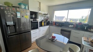 A modern kitchen with stainless steel appliances, a water dispenser, and a dining area with a glass table and chairs.