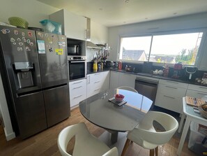 A modern kitchen with stainless steel appliances, a water dispenser, and a dining area with a glass table and chairs.