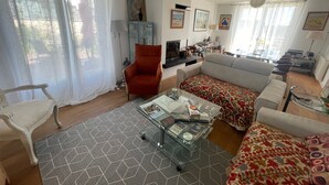 A living room with a sofa, armchair, TV, and a glass coffee table.