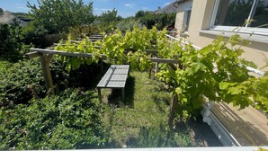 A garden with a pergola and a table, surrounded by greenery and a house.