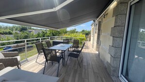 A covered outdoor patio with a table and chairs, a wicker sofa, and a stone wall.