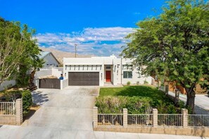 A modern two-story house with a garage, a well-maintained lawn, and a tree-lined driveway. - The Refuge - Desert Escape w/ Pool Spa & Game Room (Desert Hot Springs)