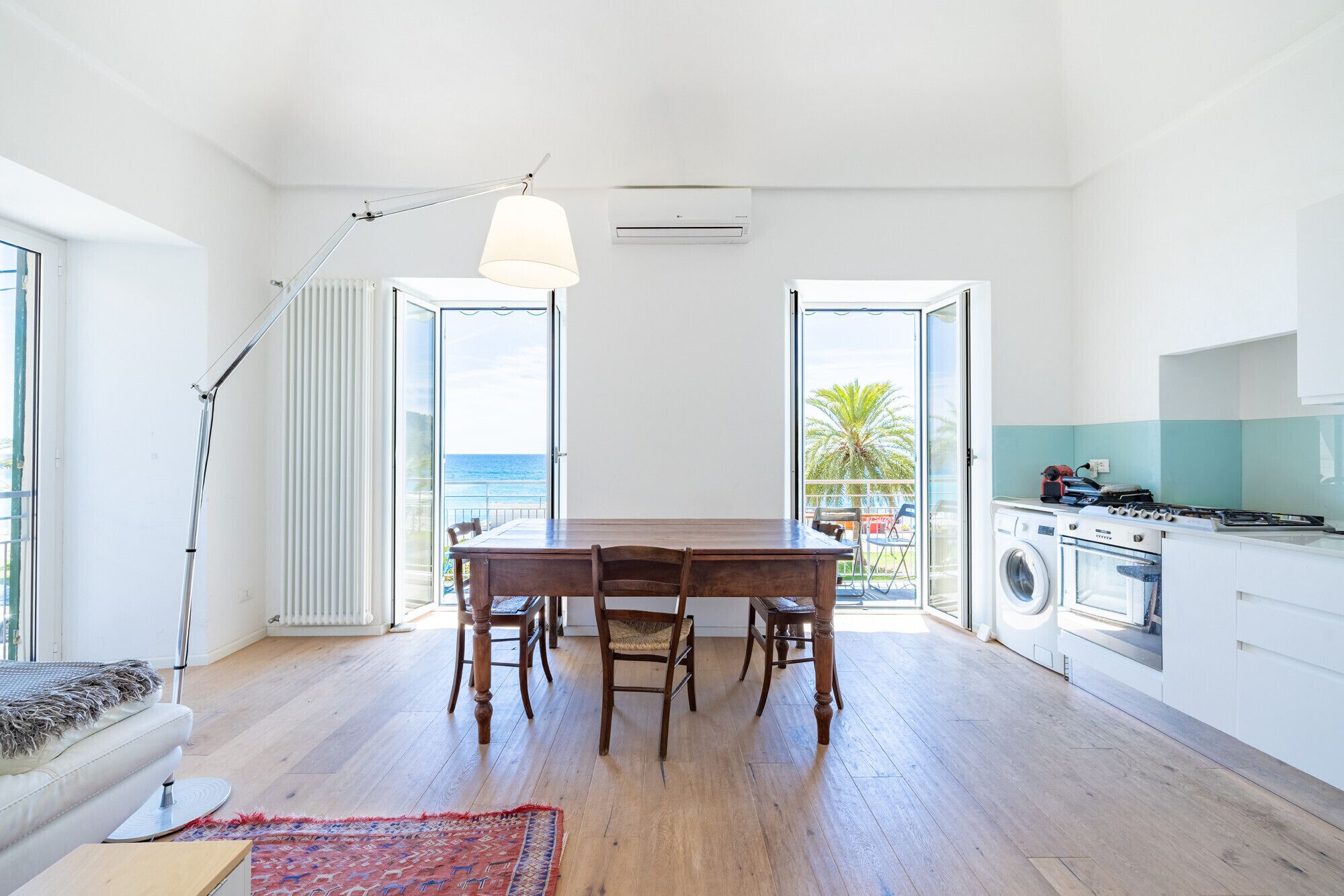 A modern kitchen with a washing machine, a dining area with a table and chairs, and a view of the ocean.
