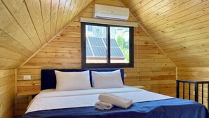 Et træhus med en seng, et vindue med solpaneler og en klimaanlæg.