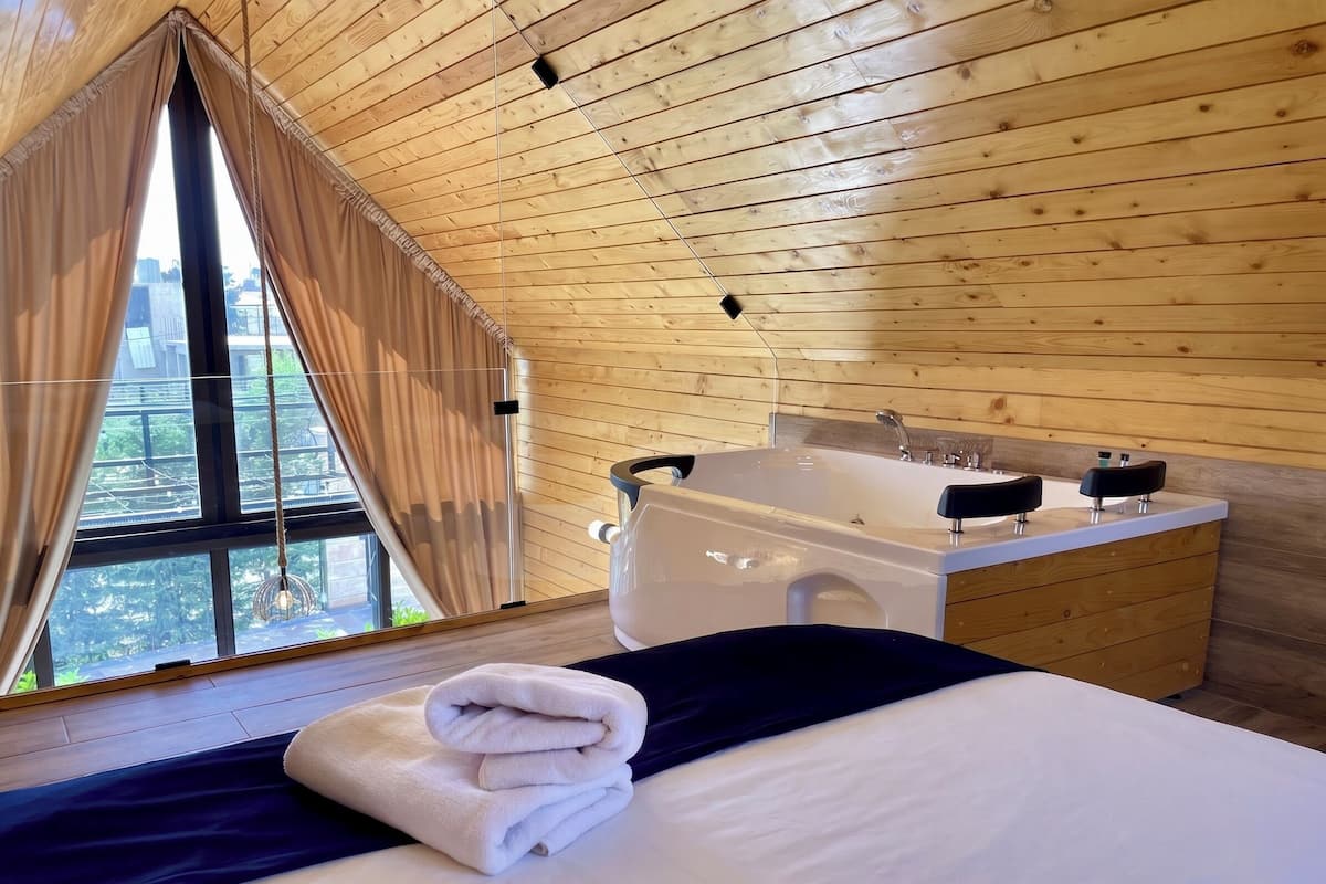 Un dormitorio con una cama grande, una ventana con cortinas, techo de madera y una bañera.