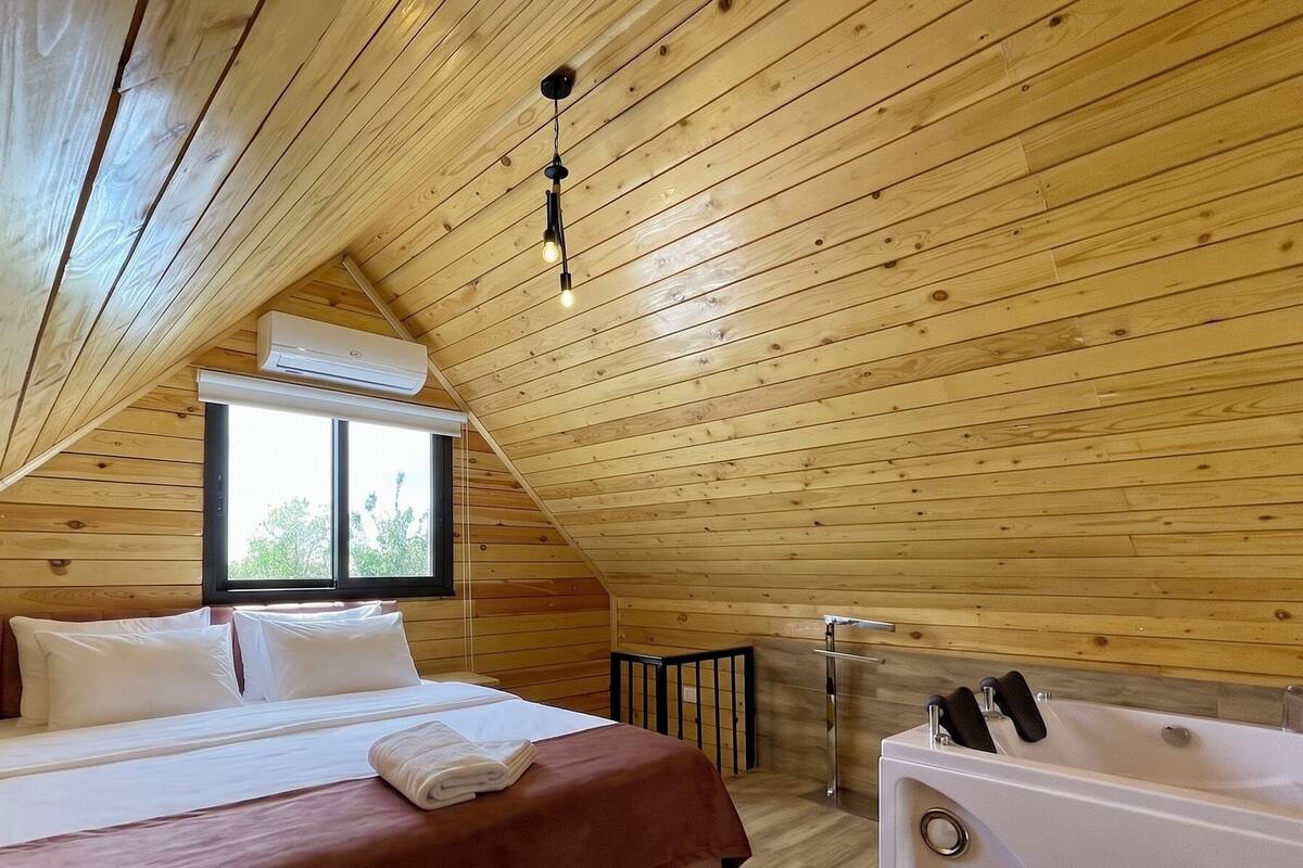 Un dormitorio con cama, ventana, bañera y techo de madera.