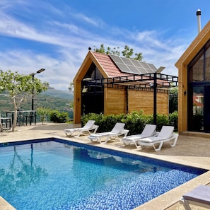 Ein Swimmingpool mit Liegestühlen, eine Holzkonstruktion mit rotem Dach und Blick auf die Landschaft.