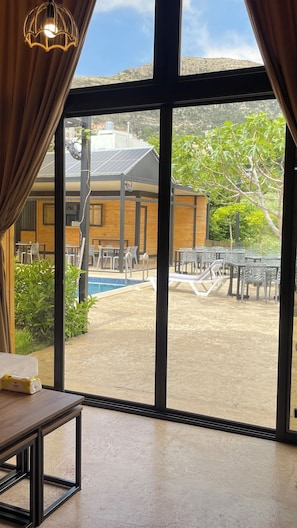 Quarto com grandes janelas, vista para piscina, área de estar ao ar livre e um edifício com painéis solares.