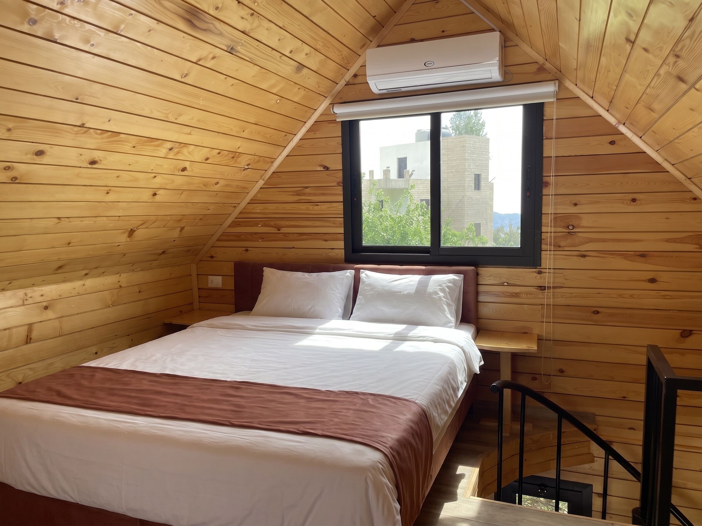 Una habitación de madera con una cama, un ventanal y un equipo de aire acondicionado.