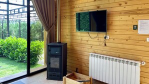 Et værelse med trævæg, et TV ophængt over en brændeovn, en radiator og et vindue med gardiner.