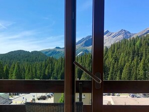 A mountain view through a window with a wooden frame and a metal handle.