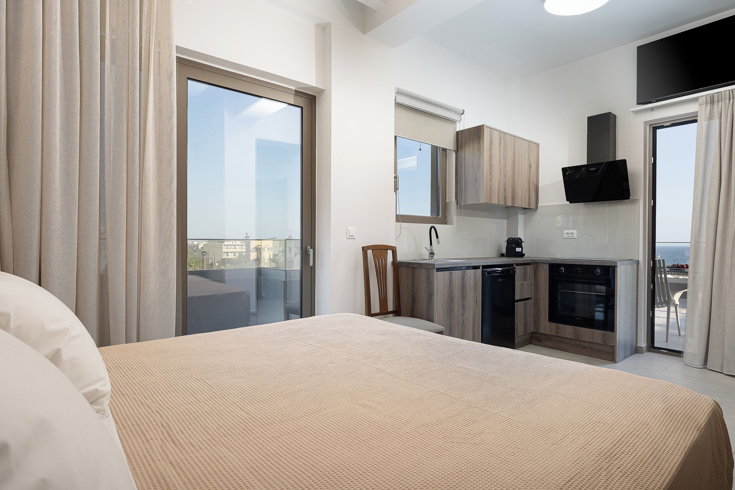 Ein modernes Hotelzimmer mit Balkon, einer Küchenzeile und einem großen Bett.