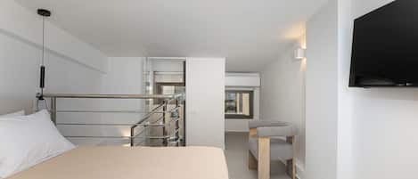 Ein modernes Hotelzimmer mit einem Bett, einem Fernseher, einem Sessel und einer Treppe, die in einen oberen Bereich führt.