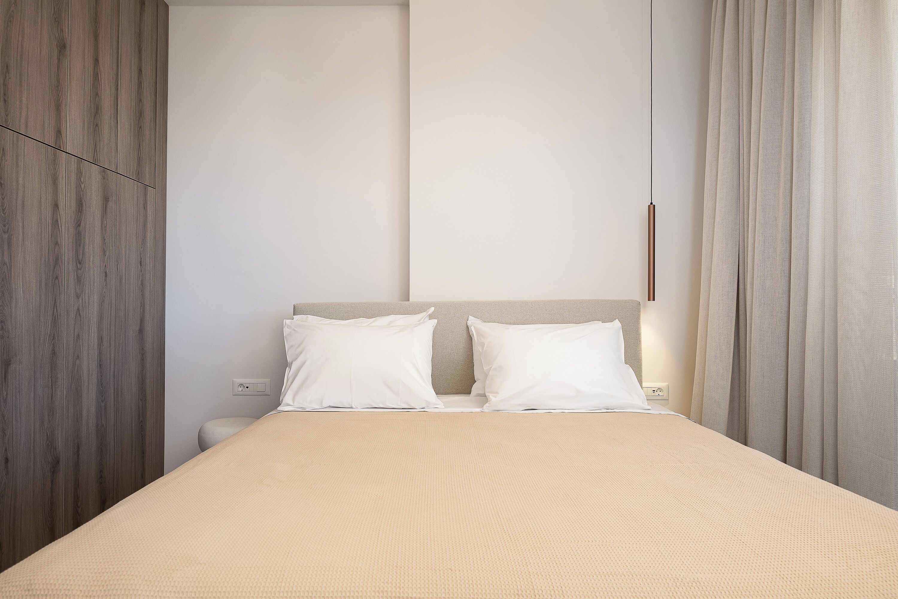 Una cama con una colcha color beige, dos almohadas blancas y un cabecero de madera.