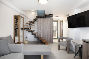 A modern living room with a staircase, grey sofa, and a flat-screen TV. - Solianna Rethymno Suites (Rethymno)