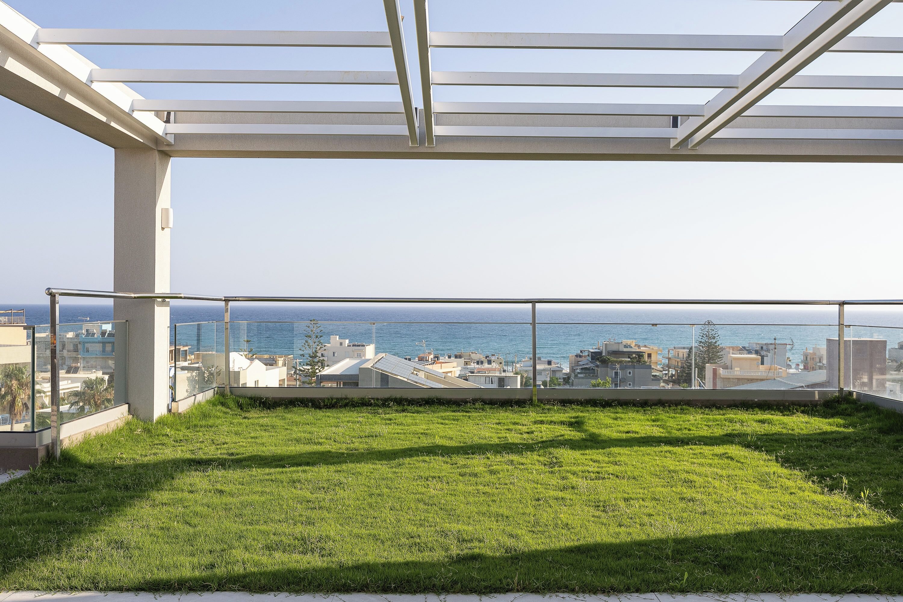 Une terrasse sur le toit dotée d’une balustrade en verre, d’un espace gazonné et offrant une vue sur la mer et le paysage urbain.