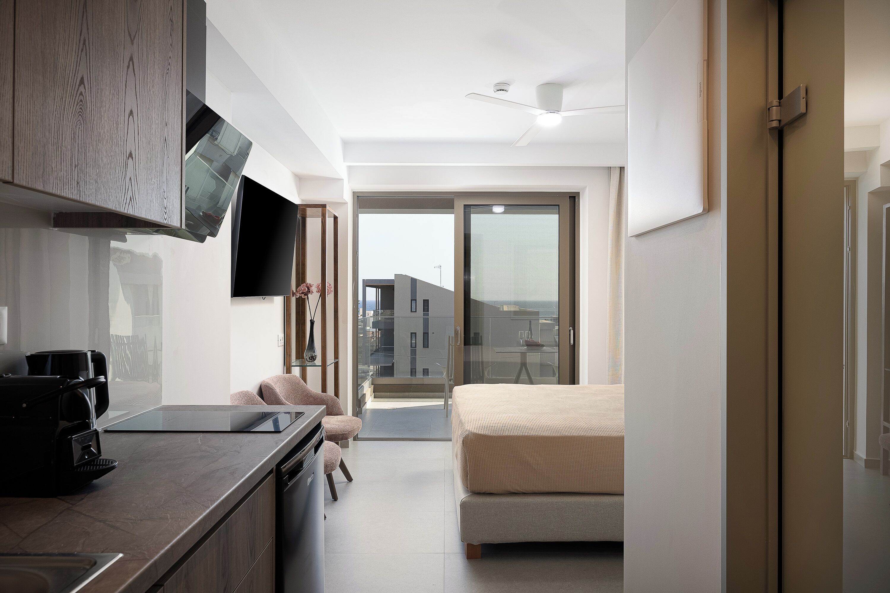 A modern hotel room with a kitchenette, a bed, a balcony, and a view of the city.