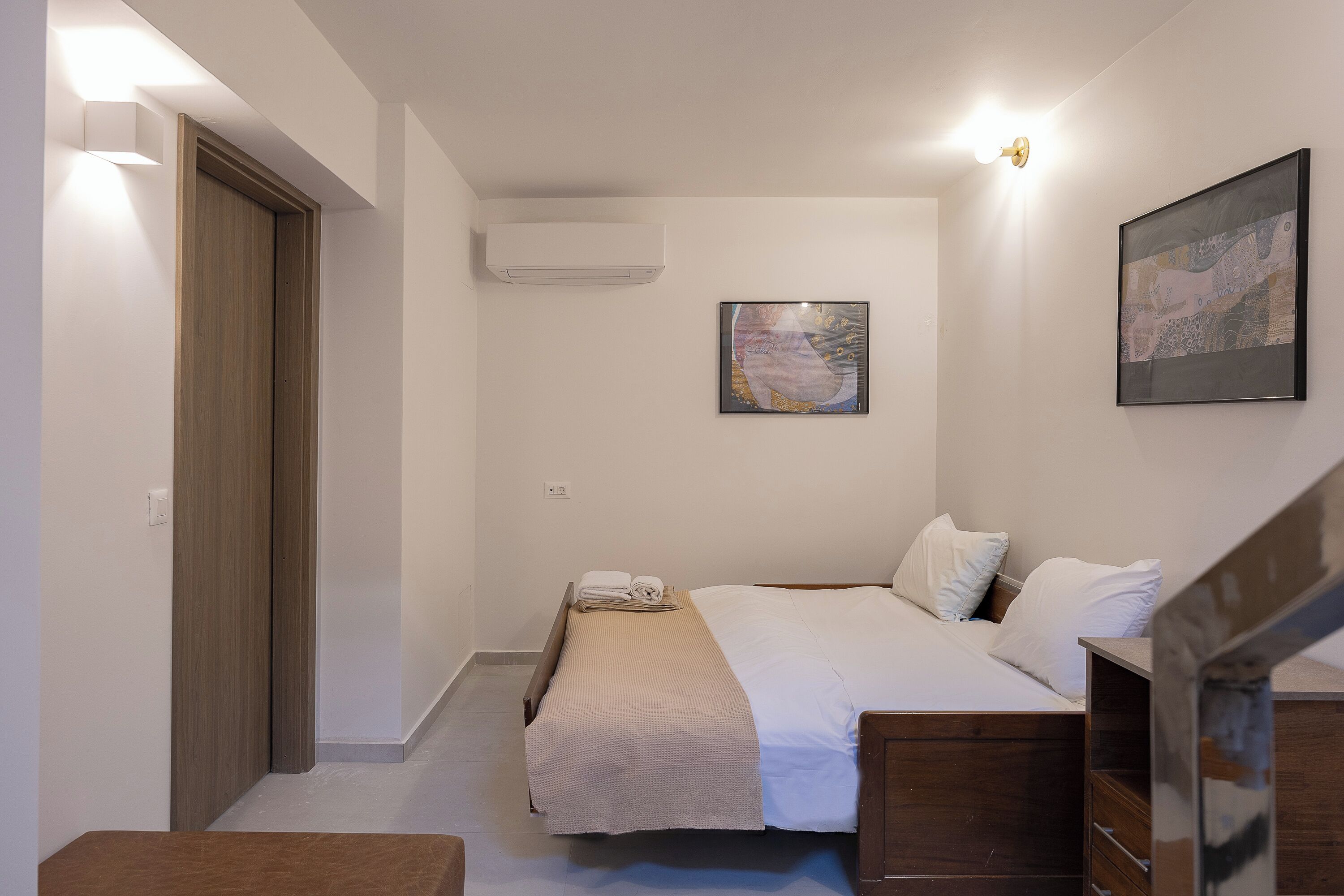 Un dormitorio con cama, un cuadro, un equipo de aire acondicionado y una puerta de madera.
