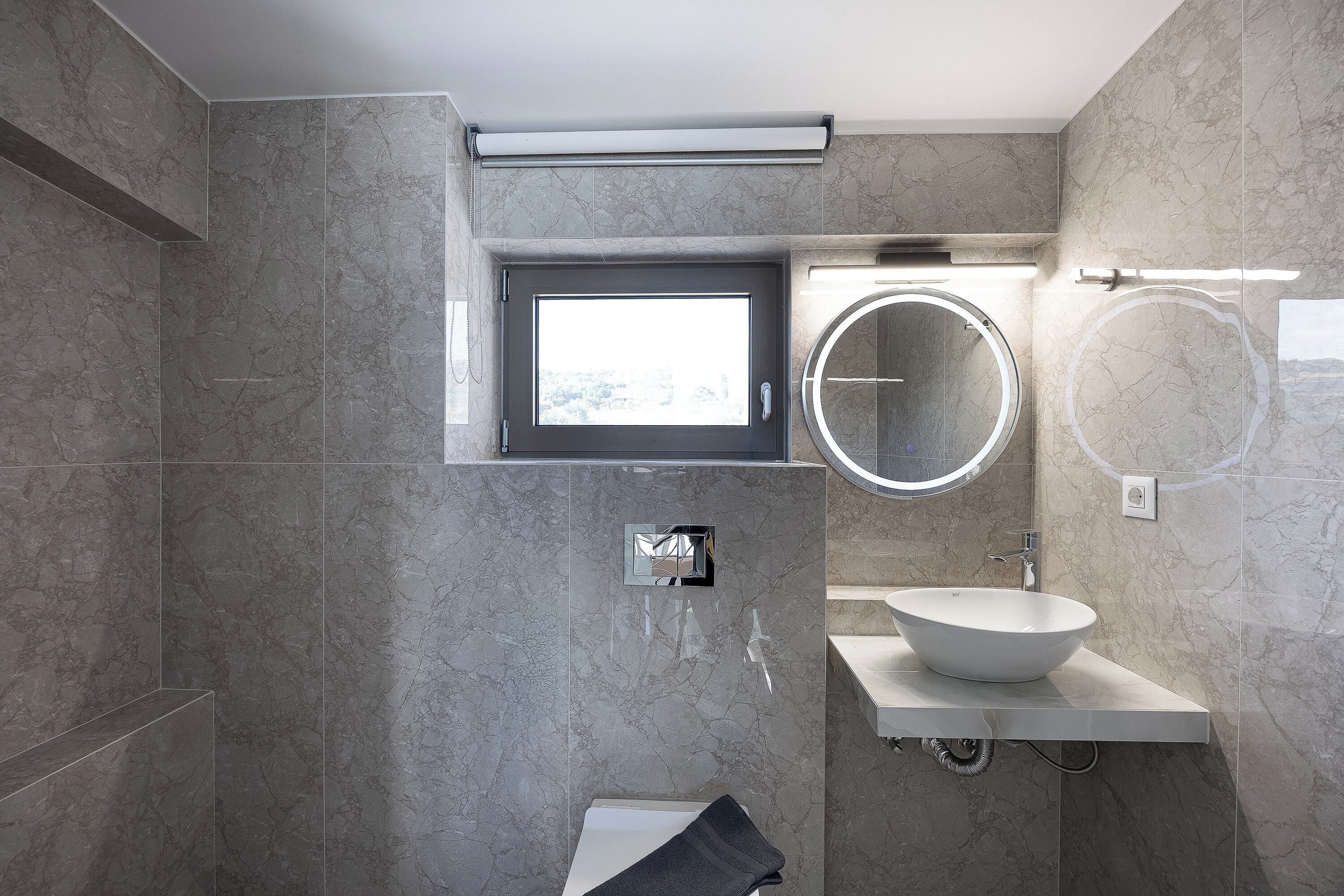 A modern bathroom with a built-in window, a round mirror, and a white sink.