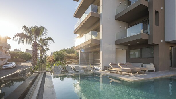 Un edificio moderno con piscina, tumbonas y una palmera.
