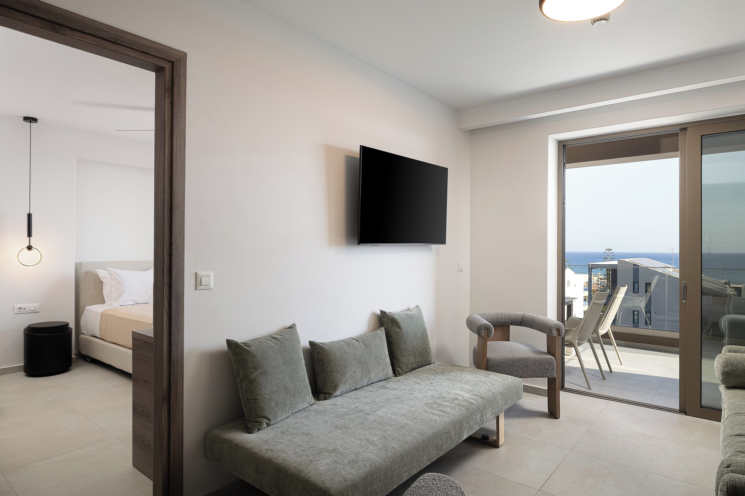 A modern living room with a sofa, a TV mounted on the wall, and a balcony with a view.