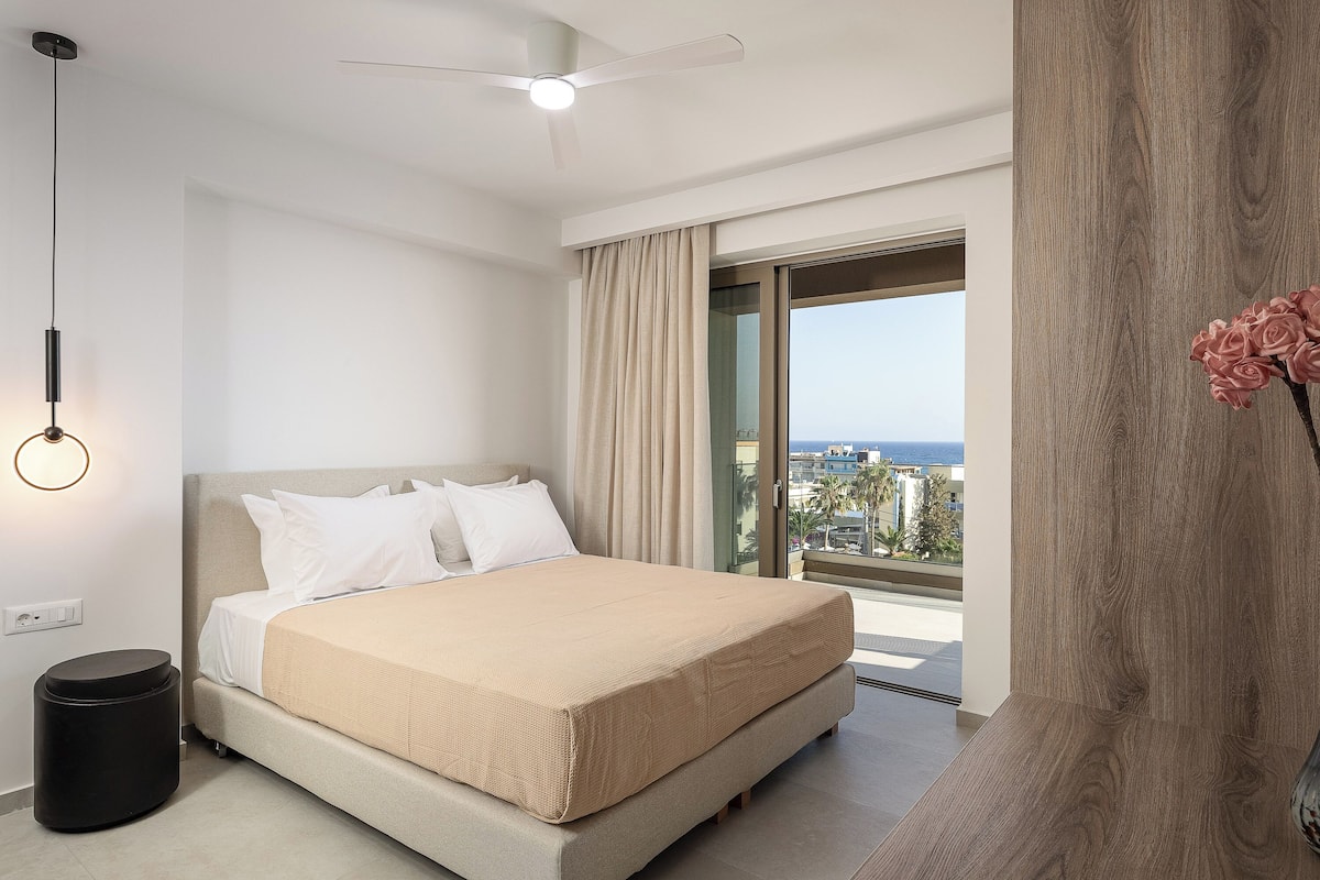 Ett modernt hotellrum med en säng, en takfläkt, utsikt över havet och ett stort fönster.