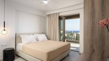 A modern hotel room with a bed, a ceiling fan, a view of the sea, and a large window.