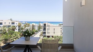 Un balcón con mesa y sillas, con vistas a una zona costera con edificios y un cielo despejado.