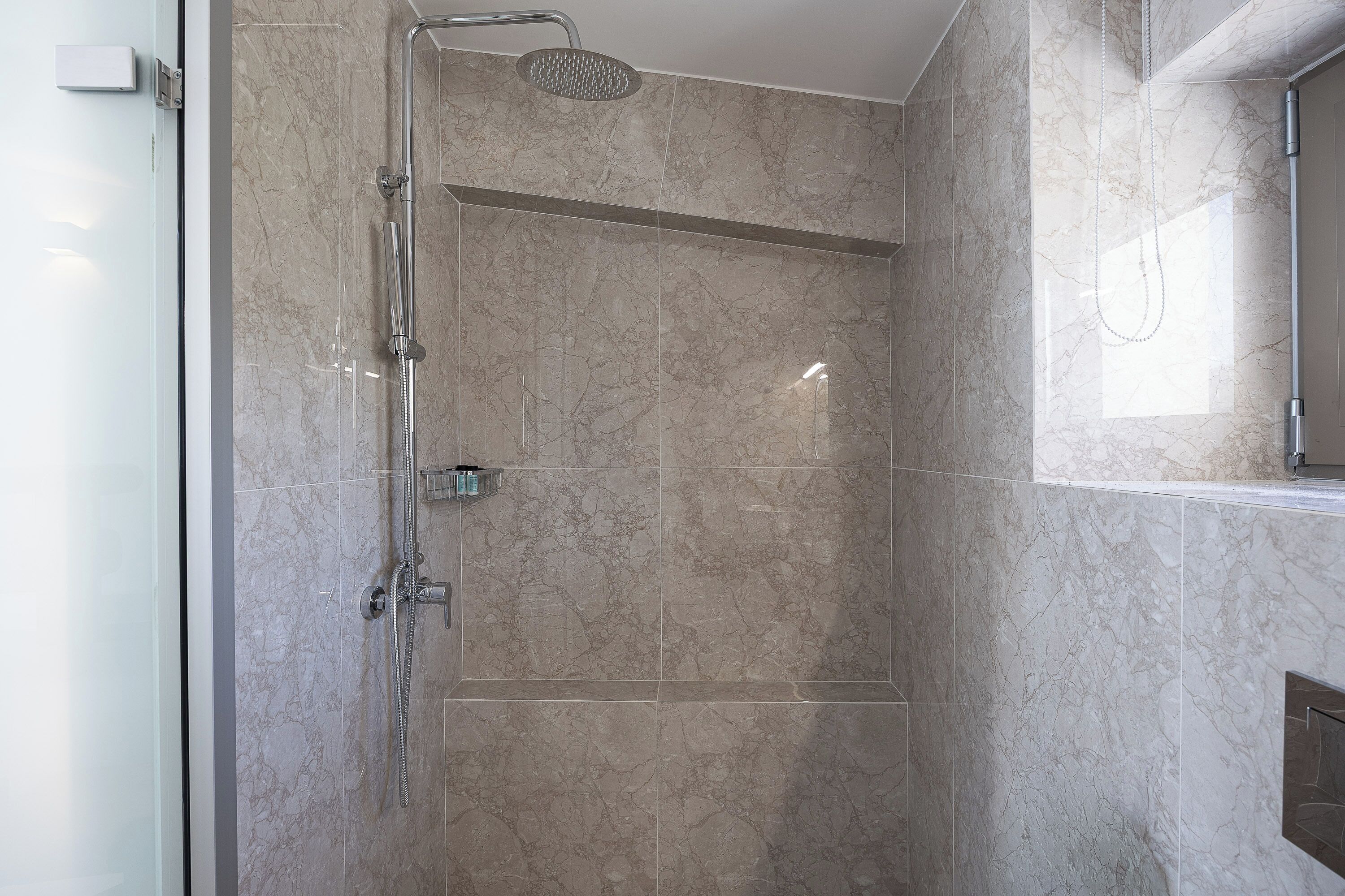 Una ducha moderna con puerta de vidrio, cabezal de ducha de mano y panel de control en la pared.