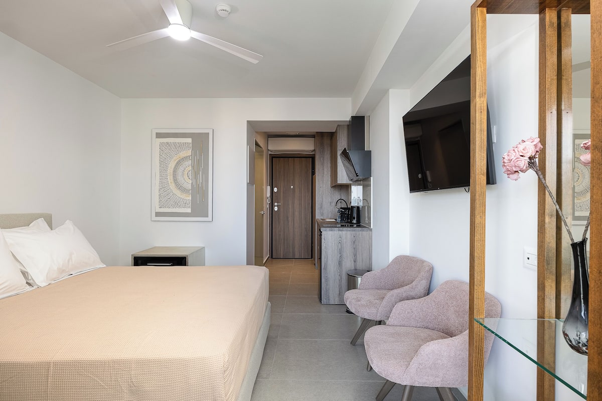 Ett hotellrum med en säng, ett skrivbord, en stol, en tv och en dekorativ vas.