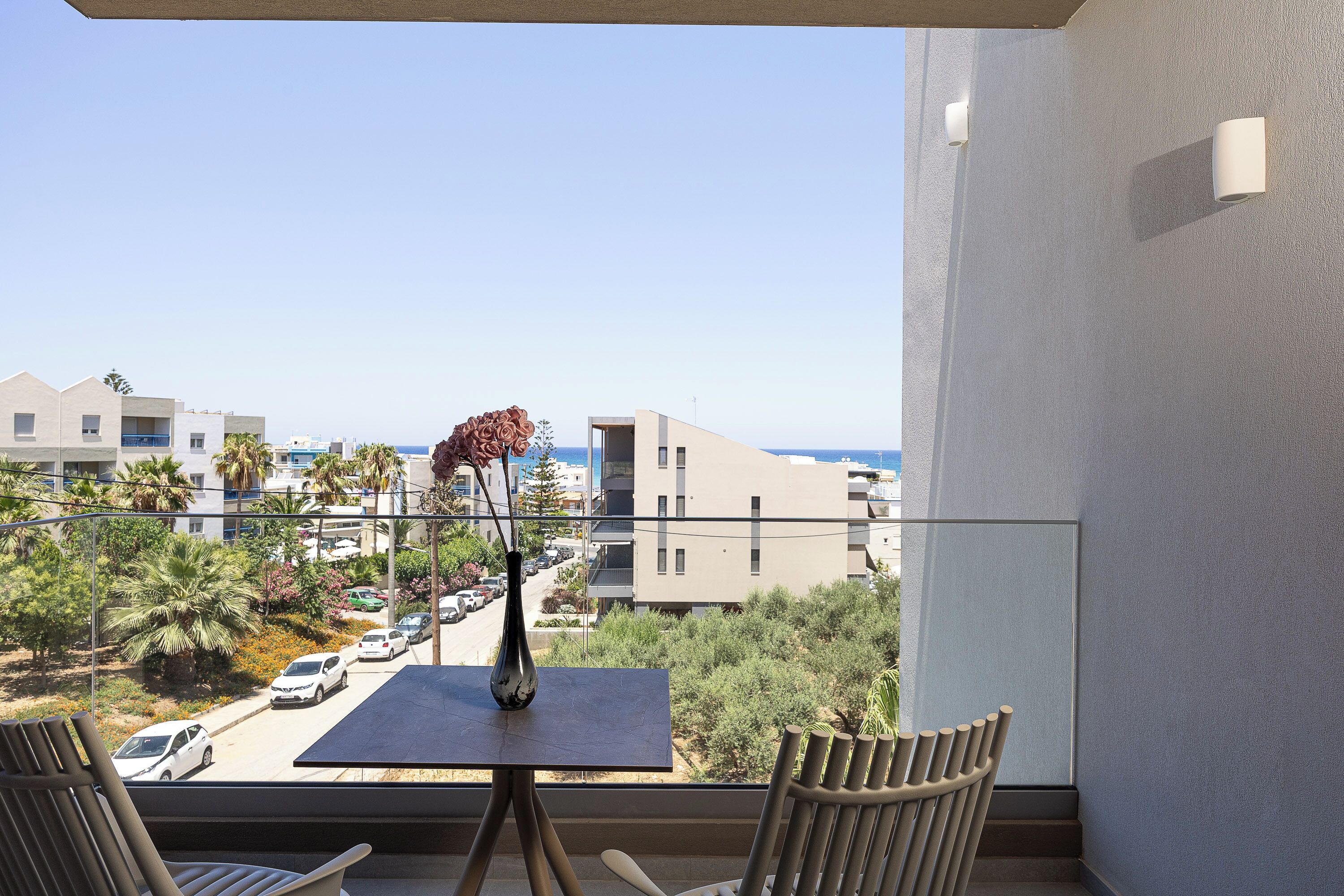 A balcony with a table, chairs, a vase with flowers, and a view of the street and buildings.