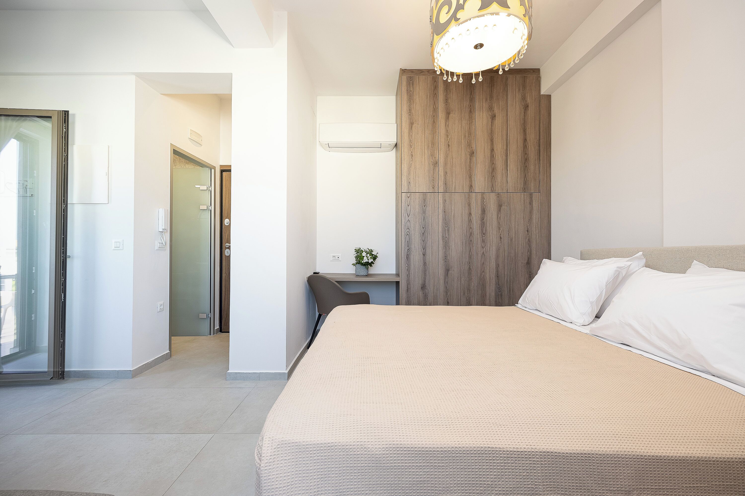 A hotel room with a bed, a desk, a chair, a plant, and a wooden accent wall.