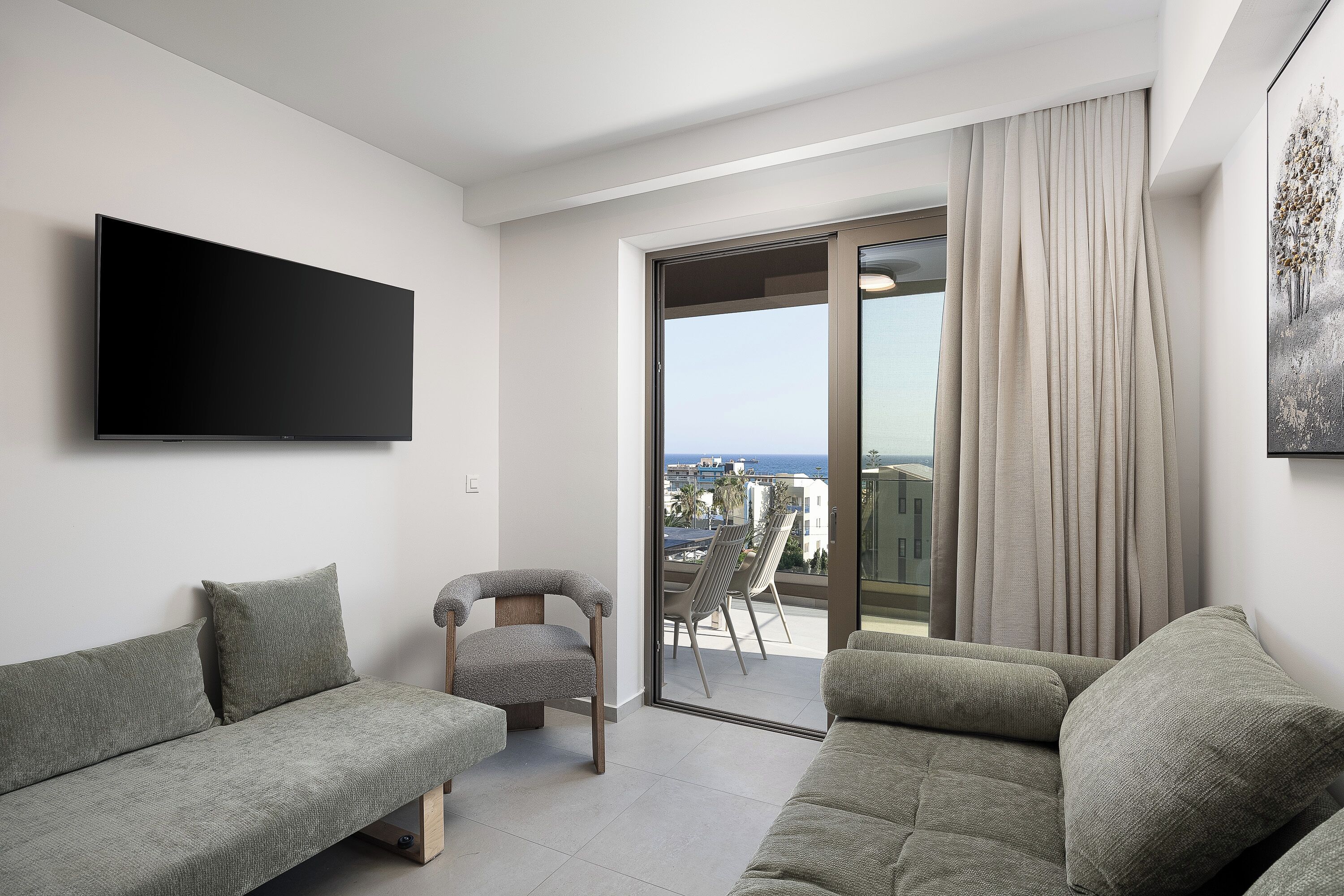 Un salon moderne doté d’un téléviseur à écran plat, de deux canapés, d’un fauteuil et d’un balcon offrant une vue agréable.