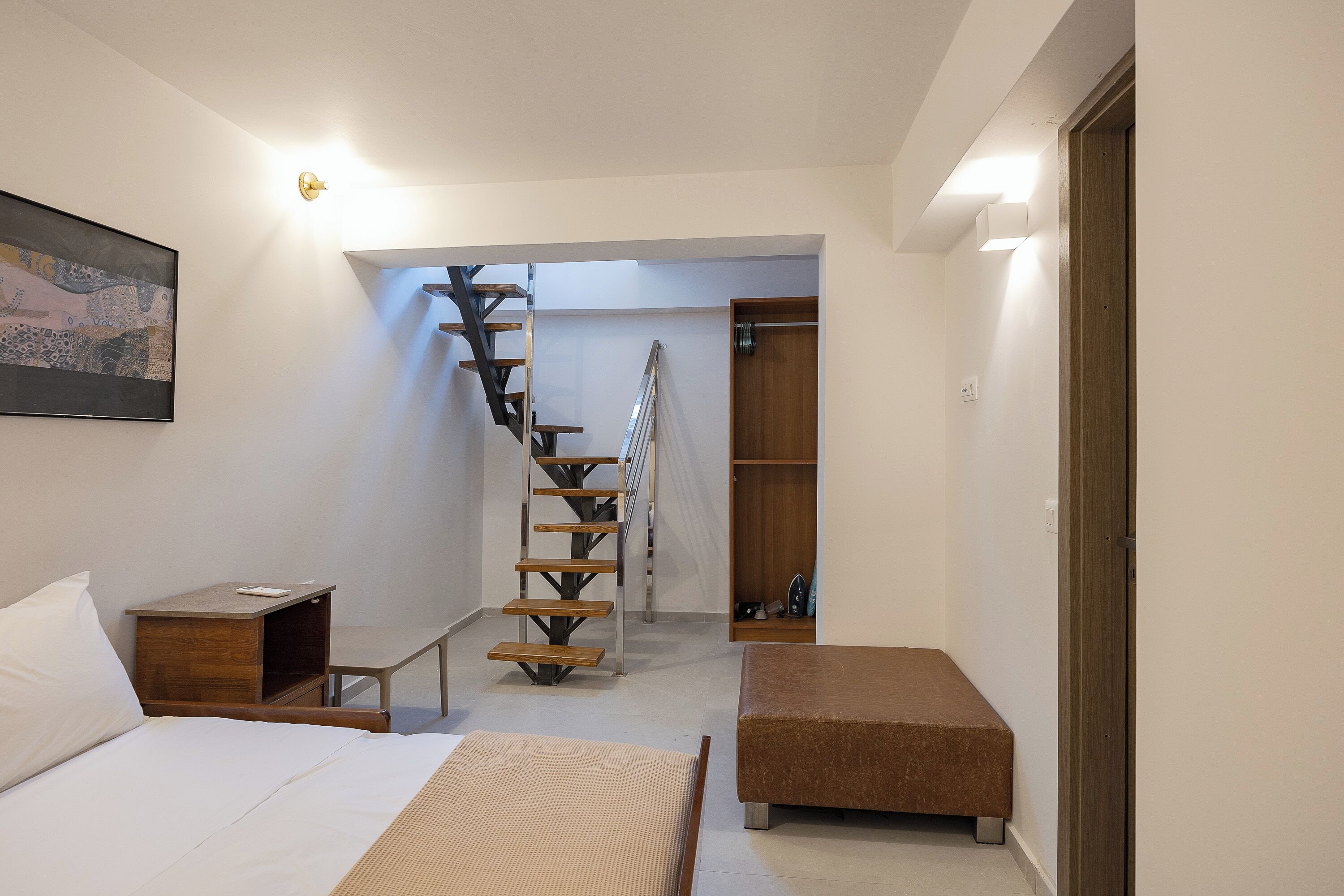 A bedroom with a bed, a bedside table, a wooden bench, a staircase, and a closet.