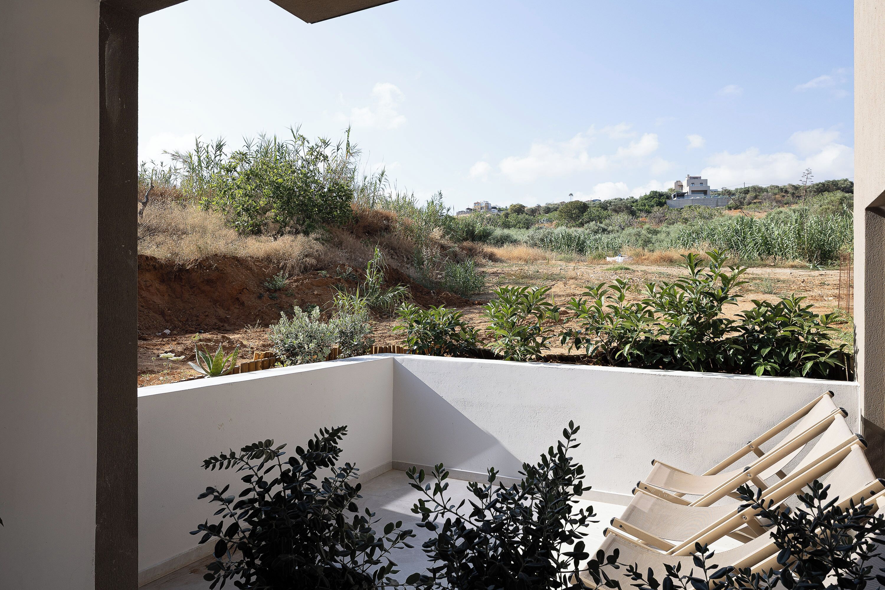 A balcony with a view of a dry landscape, a white wall, and a beige chair.