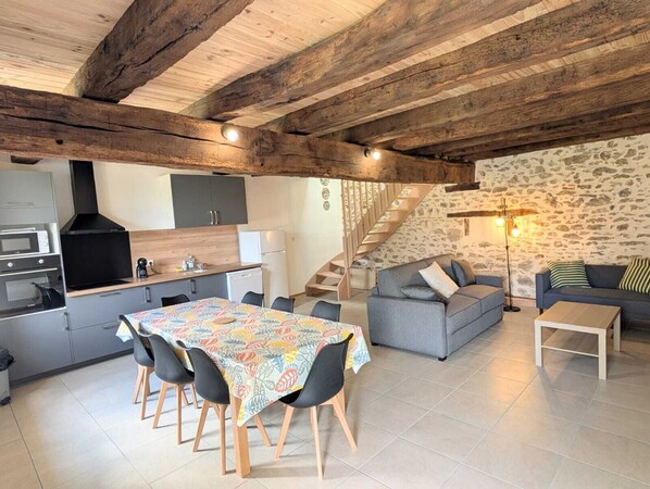 A modern kitchen with a dining area, a staircase, and a living room with a sofa and a lamp.