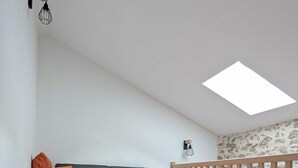 Una habitación con un sofá gris, cojines naranjas, una pequeña mesa redonda, un tragaluz y una barandilla de madera.