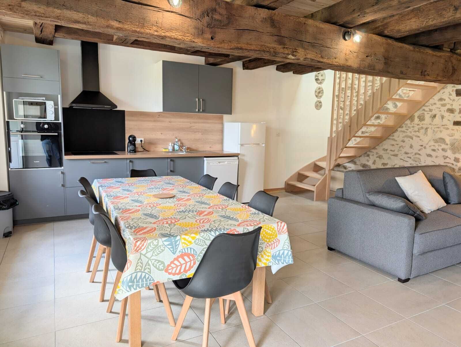 Una cucina compatta con elettrodomestici moderni, un'area pranzo con tovaglia fantasia e una scala che conduce a una zona soggiorno con divano.